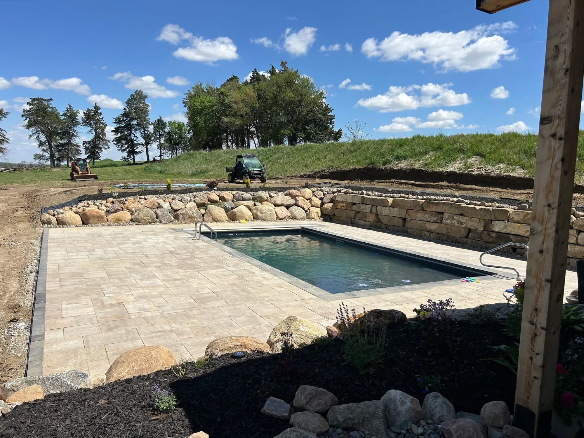 In-ground pool with paver deck and natural boulder retaining wall